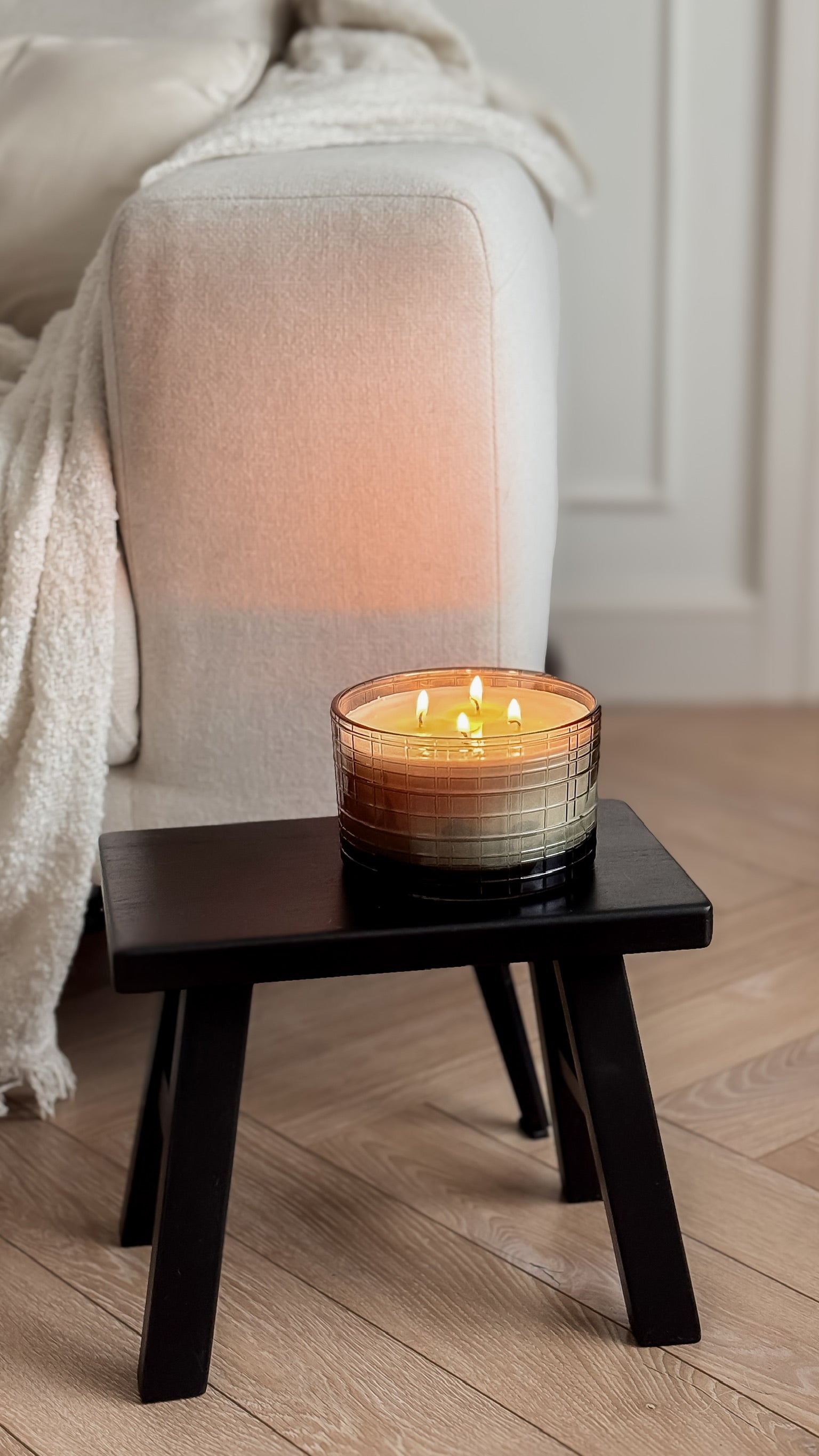 Candle on a small wooden table next to a white sofa in a room with wooden flooring.