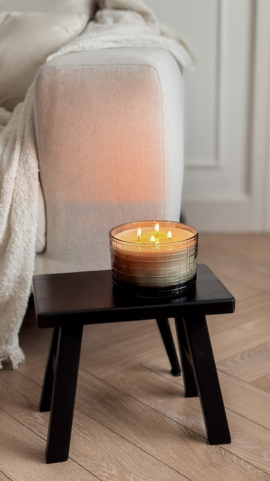 Candle on a small wooden table next to a white sofa in a room with wooden flooring.