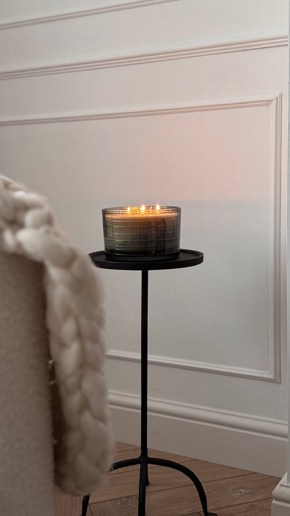 Candle on a small black stand against a white wall with wainscoting.
