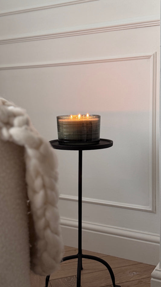 Candle on a small black stand against a white wall with wainscoting.