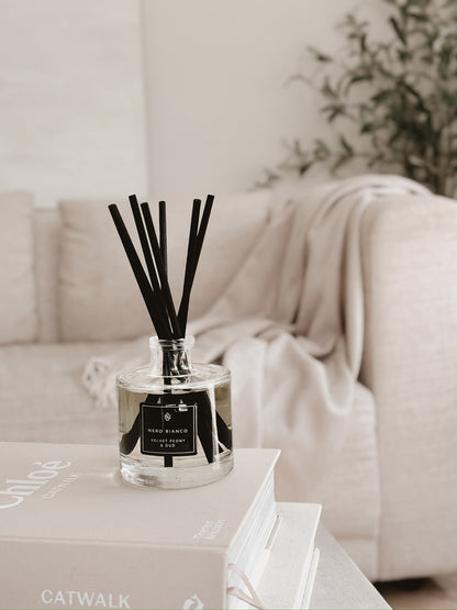 Reed diffuser on a coffee table with a blurred sofa and plant in the background