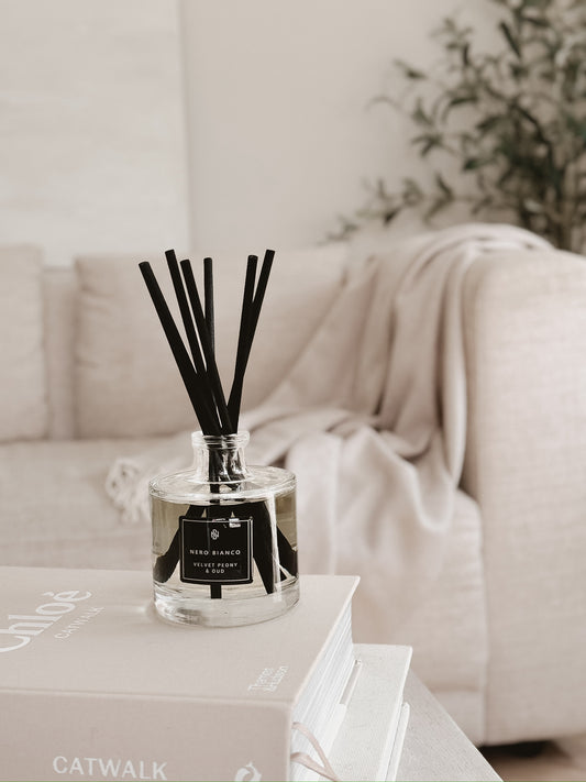 Reed diffuser on a coffee table with a blurred sofa and plant in the background