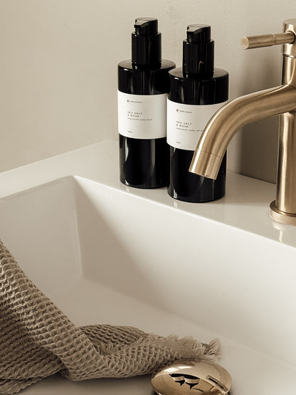 Two black bottles with white labels on a bathroom counter next to a sink and faucet.