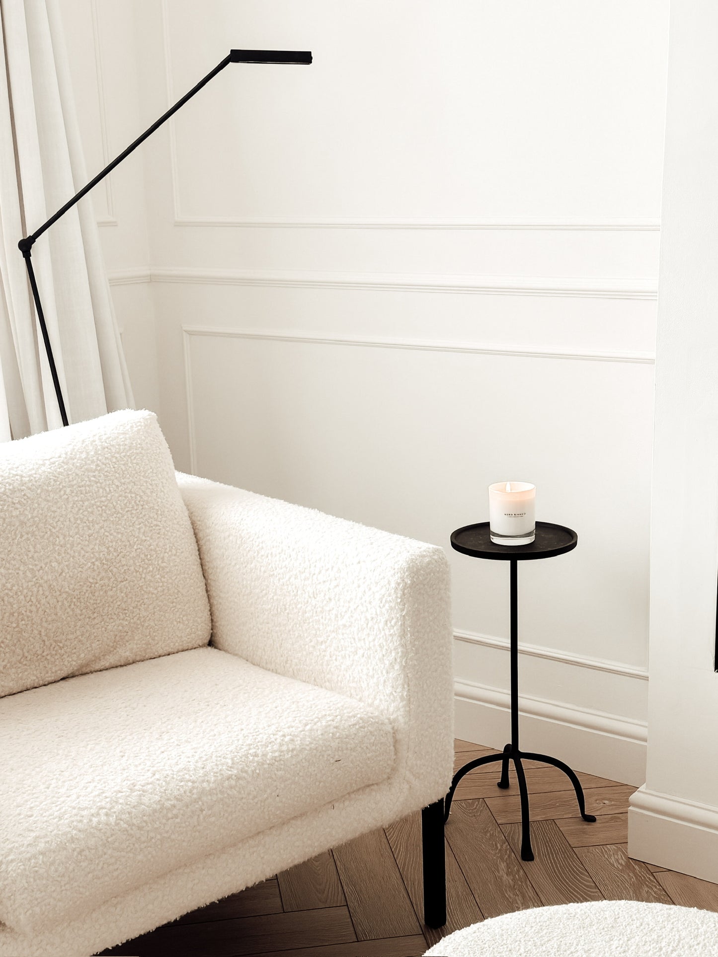 White sofa in a room with a black floor lamp and small round table with a candle.