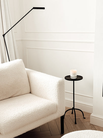 White sofa in a room with a black floor lamp and small round table with a candle.