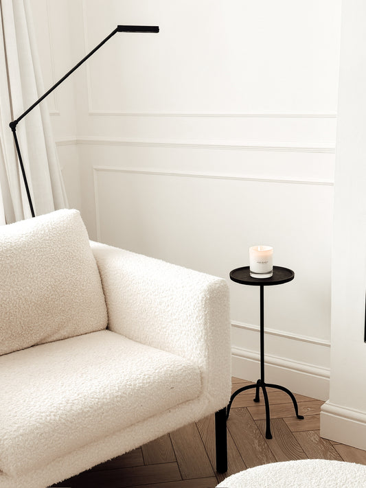White sofa in a room with a black floor lamp and small round table with a candle.