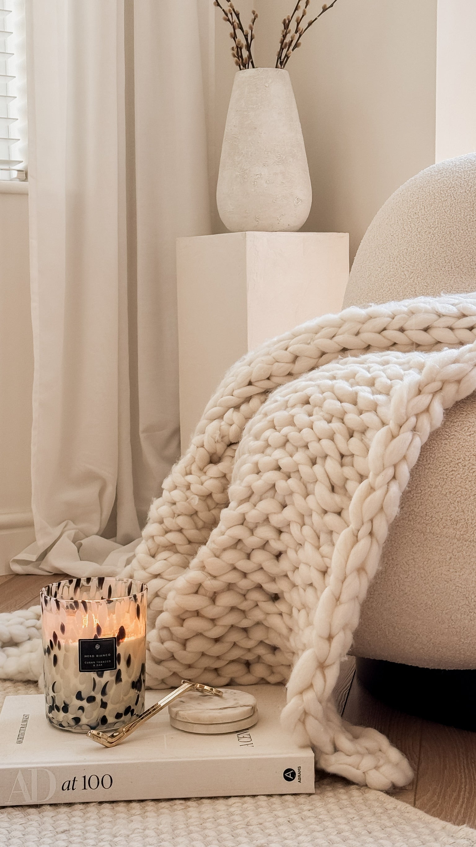 Cozy living room with a blanket, candle, and books on a sofa.