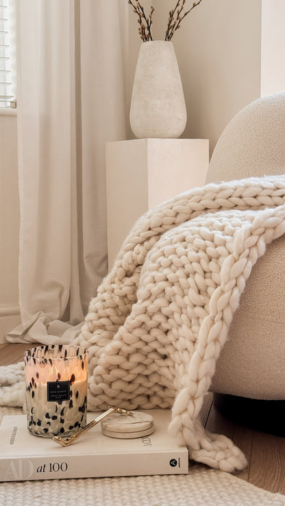 Cozy living room with a blanket, candle, and books on a sofa.