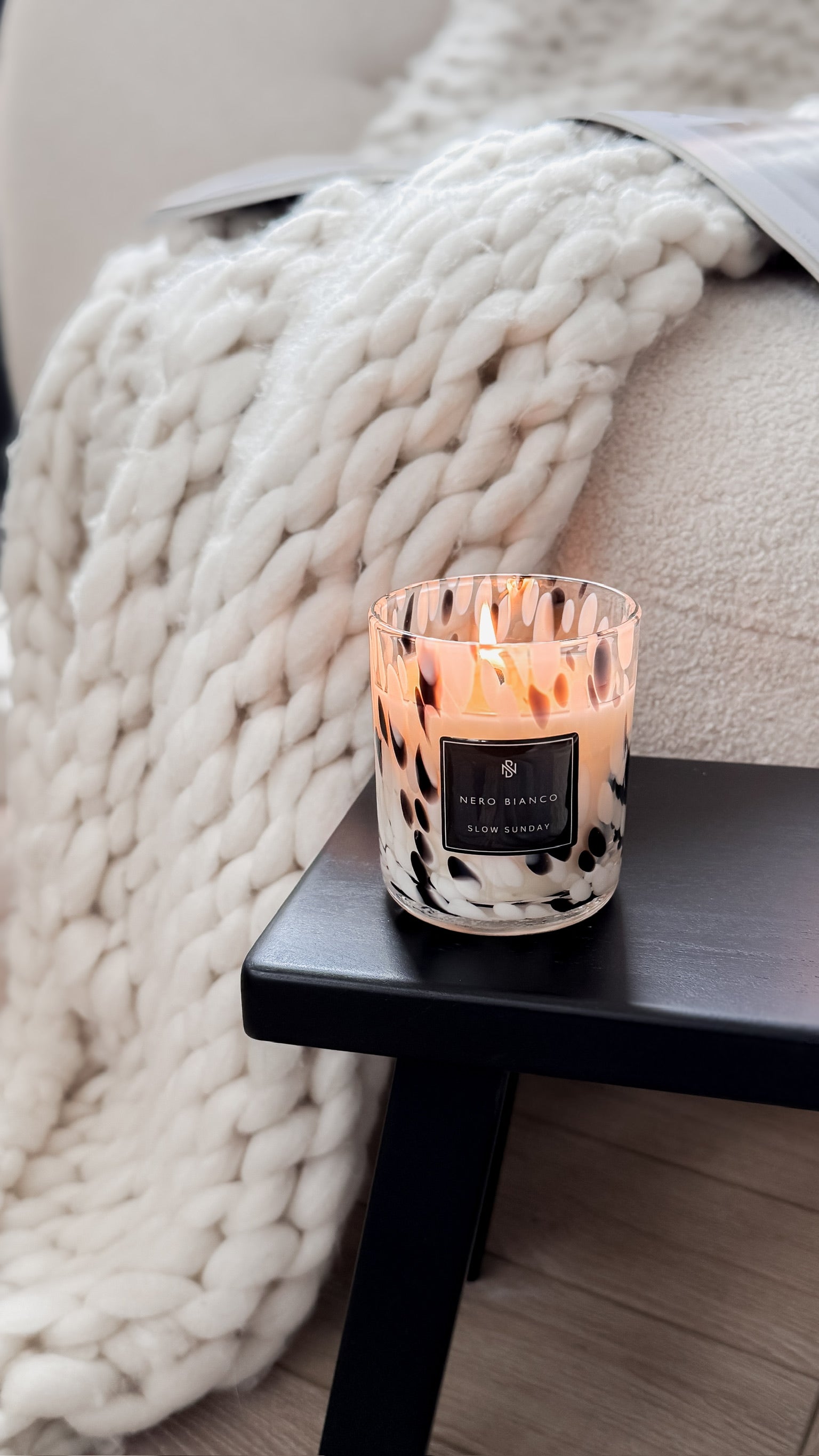 Candle on a small table with a cozy blanket in the background
