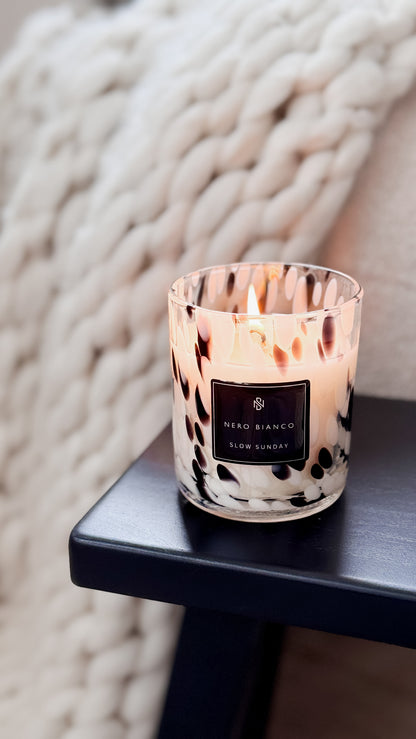 Candle with a patterned label on a dark surface against a textured white background