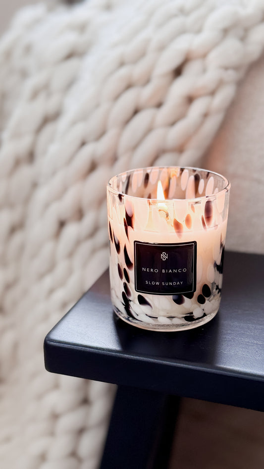 Candle with a patterned label on a dark surface against a textured white background