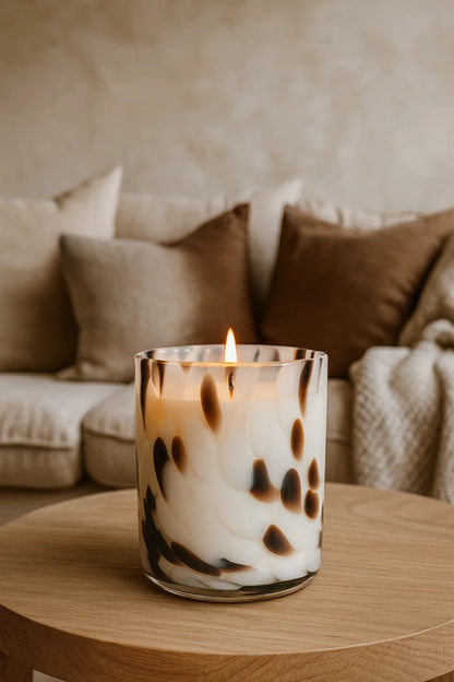 Candle in a glass holder on a wooden table with a blurred background of a cozy living room.