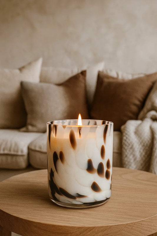 Candle in a glass holder on a wooden table with a blurred background of a cozy living room.