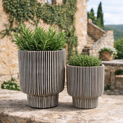 Two striped ceramic planters with green plants on a stone ledge.
