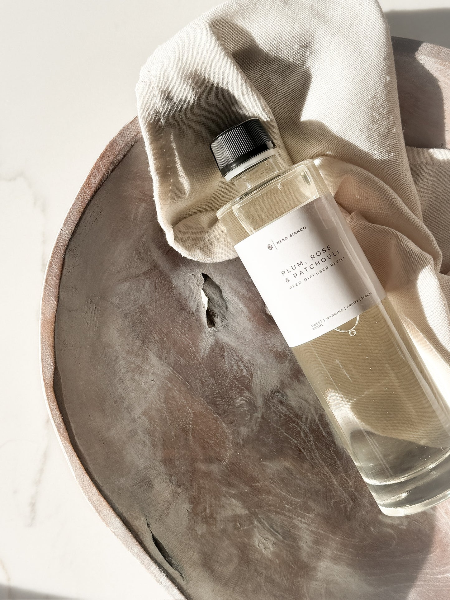 reed diffuser refill in a glass bottle with white label on a stone tray