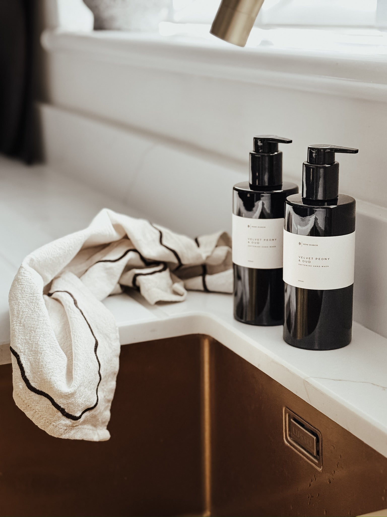 Two black bottles with pump dispensers on a bathroom counter next to a towel.