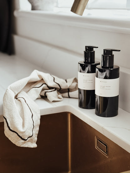 Two black bottles with pump dispensers on a bathroom counter next to a towel.