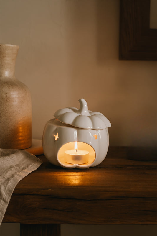 Ceramic pumpkin-shaped wax melt burmer with a lit candle on a wooden surface