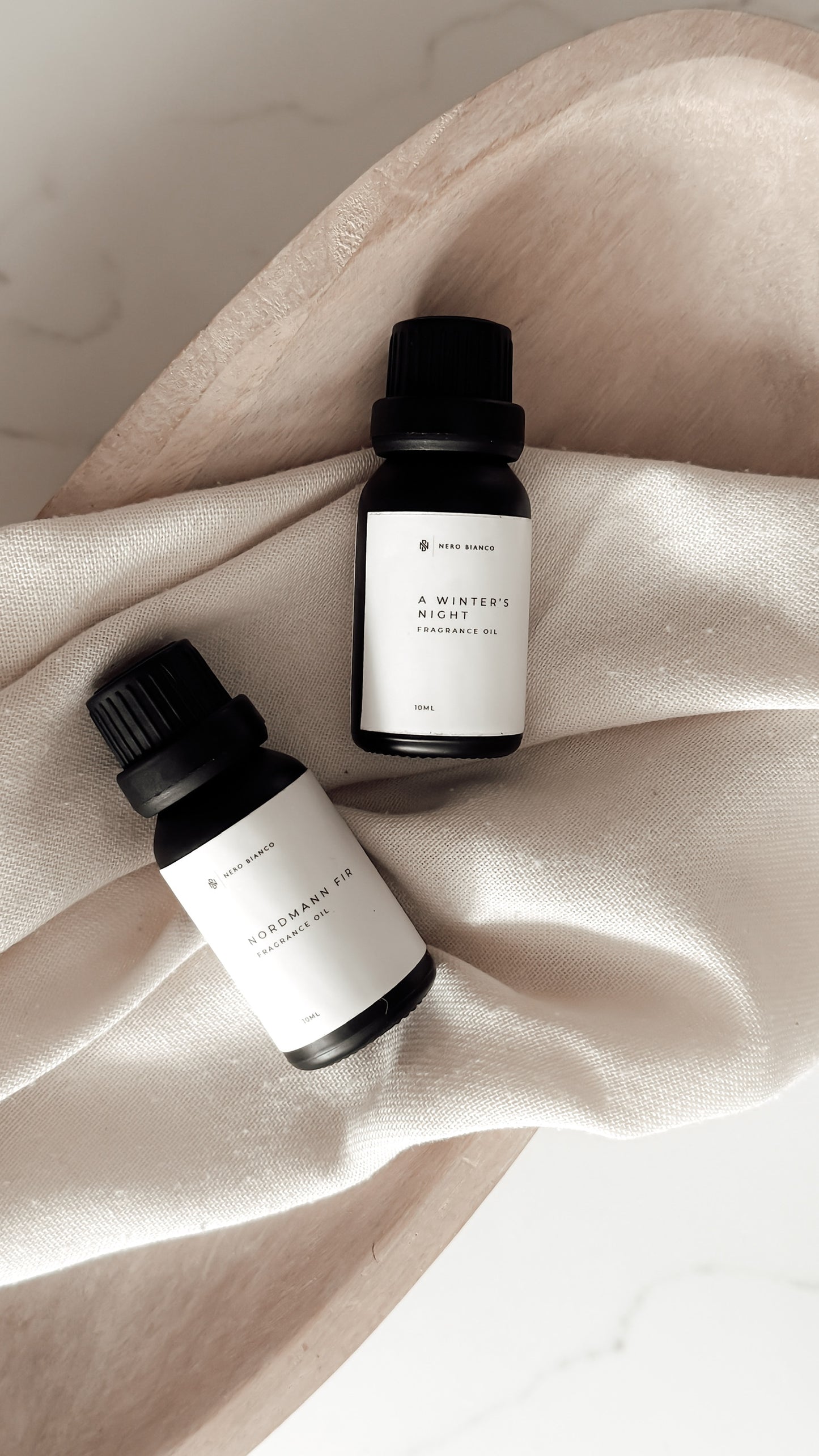 Two small bottles with black caps and white labels on a beige fabric background